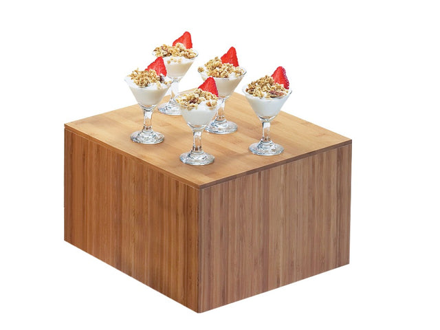Six small glass cups filled with yogurt, granola, and a strawberry slice are arranged on a Cal-Mil bamboo riser. The plain white background highlights the desserts and the cube-shaped wooden stand.