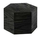 A dark, hexagonal wooden block made from oak wood with visible grain patterns is shown against a white background. The six-sided Cinderwood Riser adds a modern, geometric touch and is crafted from BPA Free materials for safety.