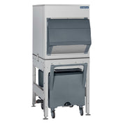 A commercial ice machine with a stainless steel body and a large, dark gray dispensing bin featuring a universal bin adapter. Set on a metal stand with a wheeled gray cart for collecting ice, it boasts generous ice storage capacity and a modern, industrial design.