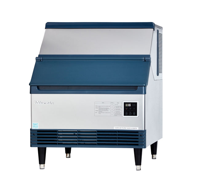 A commercial ice machine with a blue and silver exterior stands on four black legs. The front panel features a digital screen, control buttons, and a printed chart. It produces crescent style cubes, with the brand name Tilmorin displayed on the front.