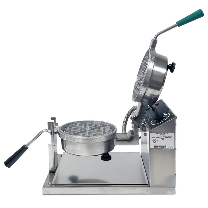 A stainless steel Belgian Waffle Baker with a round iron open at a 90-degree angle. The upright handle features a green grip, complemented by a black-handled side lever. Control buttons and a label are on the side panel.