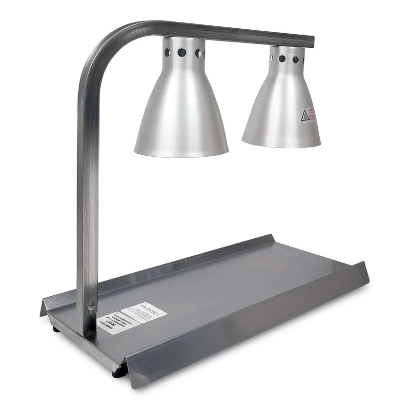 A stainless steel Warma-Serve Food Warmer with two conical heat lamps on a curved arm, positioned over a rectangular metal tray. The lamp heads feature ventilation holes and warning labels, and the base displays a product information sticker.