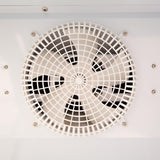 Close-up of a circular white ventilation fan with a protective grid cover, often found in Empura Refrigeration units or refrigerated merchandisers; fan blades are visible through the grid, and several screws secure the unit on a smooth, white surface.