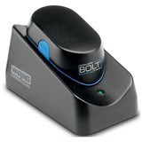 A black Waring Commercial BOLT Cordless Blender sits on its matching charging base with a green indicator light and Waring logo. The device, designed as an immersion blender, features a blue accent and a blue button on its side.