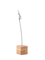 A metal alligator clip attached to a flexible wire extends from a small, square bamboo block. The object is isolated on a white background and is commonly used as a photo, card, or number card holder.