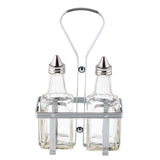 Two clear glass bottles with stainless steel tops are held upright in a rectangular metal caddy. The Oil & Vinegar Dispenser set features vertical bars and a tall looped handle for easy carrying, with both bottles empty and positioned side by side.