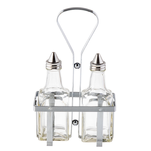 Two clear glass bottles with stainless steel tops are held upright in a rectangular metal caddy. The Oil & Vinegar Dispenser set features vertical bars and a tall looped handle for easy carrying, with both bottles empty and positioned side by side.