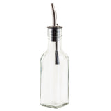 A clear, empty TableCraft 60125 Oil & Vinegar Bottle with a stainless steel pourer is attached at the top. The bottle has a simple, hexagonal shape and stands upright on a white background.