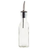 A clear, empty glass Oil & Vinegar Bottle with a square base and narrow neck, topped with a stainless steel pourer and black rubber stopper. The spout has a curved nozzle for controlled pouring, like the TableCraft 60125 used in kitchens and restaurants.