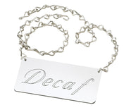 A silver chain holds a rectangular metallic tag with the word Decaf in elegant cursive script, crafted as an Urn Sign by Cal-Mil. The loosely coiled chain and reflective tag stand out against a clean white background.