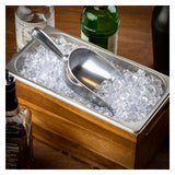 An aluminum Ice Scoop rests in a rectangular metal ice bin filled with crushed ice. The 24 oz. bin is set in a wooden holder, surrounded by assorted drink bottles on a wooden surface, suggesting a bar setup for making cocktails.