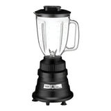 A black electric bar blender with a transparent copolyester container, handle on the right, and measurement markings. The pitcher has a lid and metal blade inside. The base features control buttons and stands on four small legs against a plain white background.