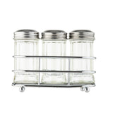 Three empty glass shakers with stainless steel tops are arranged side by side in a silver metal rack. The jars have a classic, clear design, and the simple wire rack rests on small round feet. The background is white and uncluttered.