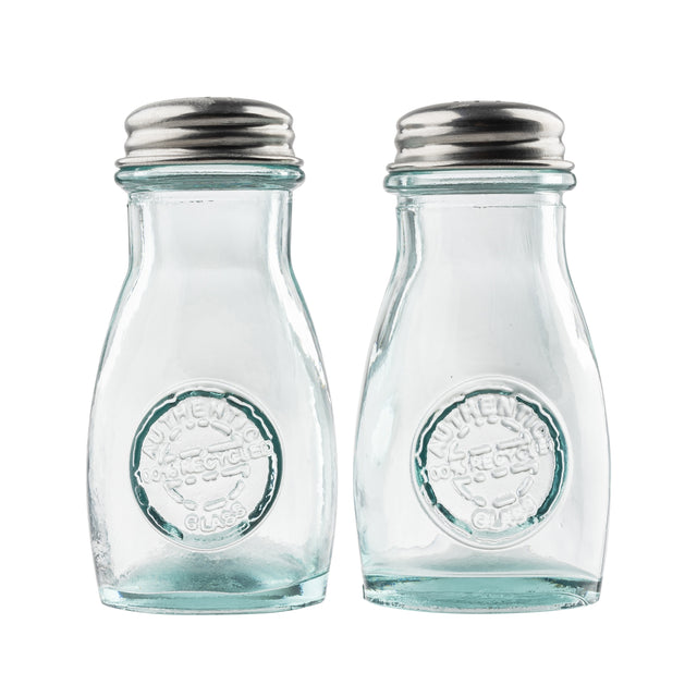 Two empty, clear recycled glass jars with stainless steel tops are side by side. Each shaker has a round embossed logo on the front reading Authentic Recycled Glass. The background is plain white, and the shakers are clean and unused.