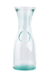 A tall, clear authentic carafe with a narrow neck and wide mouth. Crafted from recycled glass with a subtle green tint, it holds 28 oz. The slightly thicker bottom and embossed circular seal add elegance against a plain white background.