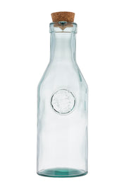 A clear apothecary bottle made of recycled glass features a round embossed seal on the front and is topped with a natural cork stopper. Its narrow neck widens at the base, set against a plain white background to highlight its simple design.