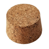 The TableCraft Products 6631 Cork Stopper features a cylindrical shape with a wider top and narrower base, made from compressed tan cork. Its rough, porous surface has visible small holes and cracks, isolated on a white background.