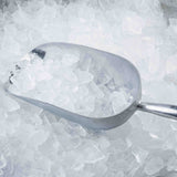 An aluminum Ice Scoop, 85 oz in size, is filled with small, clear ice cubes and rests atop a larger pile of ice. The sturdy scoop has a shiny, reflective surface and handle, enhancing the cold and frosty atmosphere of the scene.