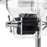 Close-up of a stainless steel cereal dispenser spigot, featuring a metallic cross-shaped handle on a clear container with beveled edges. Inside, a black paddle-type mechanism is visible against a clean, white background.