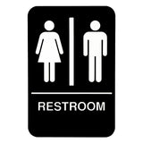 A black rectangular ADA compliant restroom sign features white icons: a female figure in a dress on the left, a male figure in pants on the right, separated by a vertical line. "RESTROOM" is written below in bold uppercase letters, with Braille included.