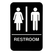 A black rectangular ADA compliant restroom sign features white icons: a female figure in a dress on the left, a male figure in pants on the right, separated by a vertical line. "RESTROOM" is written below in bold uppercase letters, with Braille included.