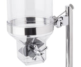 A close-up of a clear polycarbonate beverage dispenser with a cylindrical container, shiny metal accents, and a cross-shaped metal spigot handle attached to a vertical metal stand. The image focuses on the lower half and dispensing mechanism.