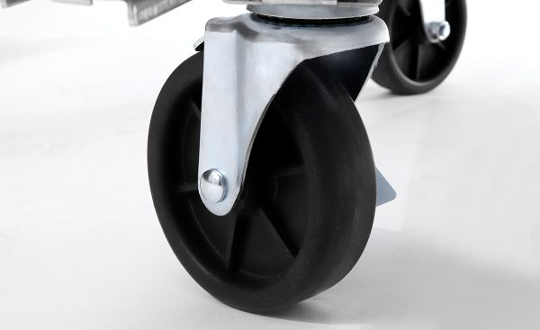 Close-up of a black caster wheel with a metal bracket, attached to the bottom of an Atosa MBB69GGR Back Bar Cooler or similar piece of equipment, on a smooth white surface. The wheel has a solid black center and is positioned at an angle, with another wheel visible behind it.