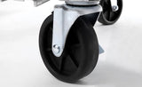 Close-up of a black caster wheel with a metal bracket, attached to the bottom of an Atosa MBB69GGR Back Bar Cooler or similar piece of equipment, on a smooth white surface. The wheel has a solid black center and is positioned at an angle, with another wheel visible behind it.