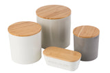 Four minimal, modern canisters with bamboo lids are grouped together. Three upright melamine canisters in white, light gray, and dark gray stand beside a rounded rectangular white container labeled “BUTTER ALL THE THINGS.”.