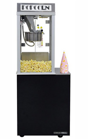 A vintage-style popcorn machine filled with popped popcorn, sitting on a black equipment base with doors. A metal popping kettle is inside the glass case, and a single striped popcorn cone is placed on the right side of the stand.