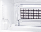 Close-up of a stainless steel icemaker inside a freezer, featuring a grid of square molds and metallic components. To the left, a frosted glass bottle stands upright against the white interior wall, highlighting clear ice production.
