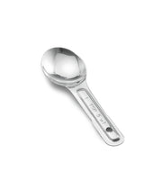 A single stainless steel measuring spoon is shown on a white background. The handle is flat with a hole at the end and engraved with “1 TBS / 15 ml.” The spoon has a round, polished bowl and a shiny, reflective surface.