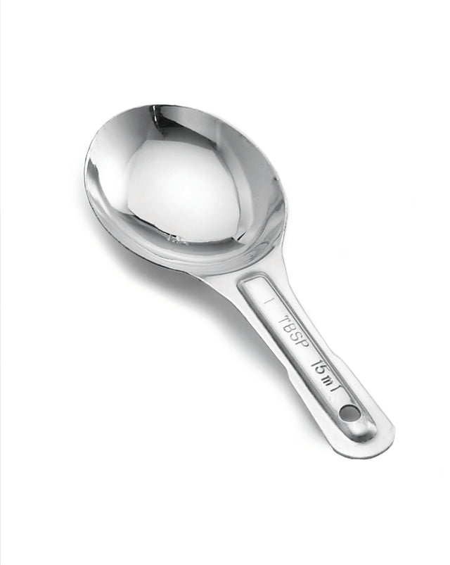 A shiny stainless steel measuring spoon with a short handle is shown on a white background. The handle is stamped with measurement markings: 1 TBSP and 15 mL. A small hole at the end allows for hanging, and it is dishwasher safe.