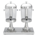 Two large, clear beverage dispensers with stainless steel lids and bases are mounted side by side on a shared tray with drip grates. Each dispenser has a black spigot at the bottom and is dishwasher safe for easy cleaning.