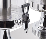 Close-up of a stainless steel and black plastic beverage dispenser spigot attached to a clear container. The handle is upright, reflective surfaces capture light, and another dispenser appears to the right against a white background.