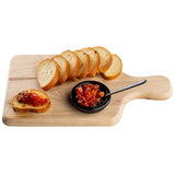 A natural finish wood bread board holds six slices of toasted baguette, a black dish of tomato bruschetta with a small spoon, and one baguette slice topped with bruschetta. The background is white. Perfect for your TableCraft presentation.