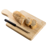 A wood bread board with a loaf of bread, two slices cut, and a bread knife with a black handle rests on it. The board features a handy knife slot, all arranged neatly against a white background.