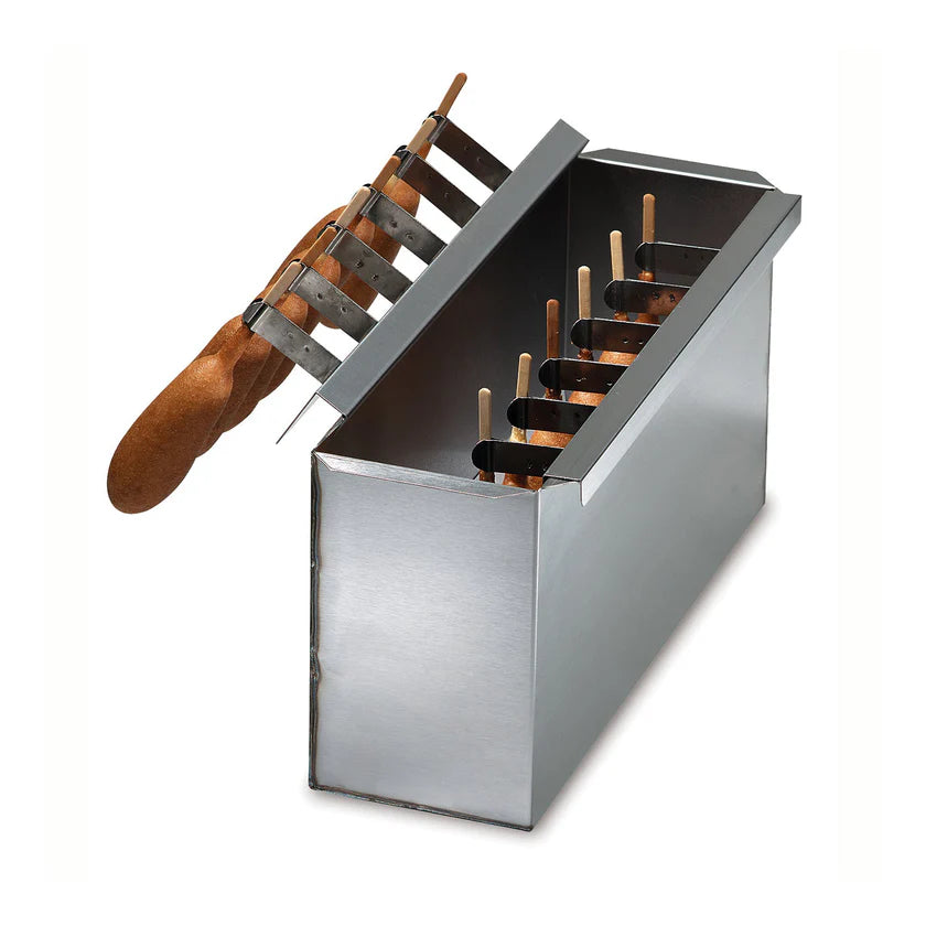A rectangular stainless steel batter dip tank for making treats like corn dogs or ice cream bars, with a hinged lid partially open, showing wooden sticks in the dark liquid. A wooden-handled tool with metal tines rests on top. Background is plain white.