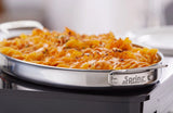 A 1-1/2 qt. oval stainless steel pan labeled “Spring” contains baked pasta topped with melted orange cheese and sprinkled herbs, sitting on a black stovetop. The crispy, golden edges make it perfect for a buffet sauté presentation.