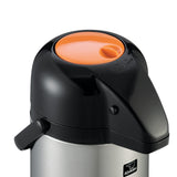 A close-up of a Zojirushi stainless steel airpot with a black lid and handle. The round lid features an orange top and spout, plus a black push-button for dispensing. Its stainless steel vacuum liner ensures excellent heat retention. The logo is visible on the front.