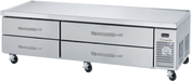 A stainless steel refrigerated chef base with four horizontal drawers and a right-side ventilation panel sits on caster wheels. The flat surface is ideal for prepping food, making it a versatile equipment stand in restaurant kitchens.