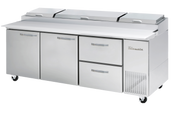 A large, three-section stainless steel Pizza Prep Table features a white cutting surface, three storage compartments, two pull-out drawers, overhead lid covers, and ventilation grates on the right, all mounted on caster wheels for easy mobility.