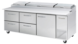 A large stainless steel refrigerated prep table with six handles: four drawers on the left, a door on the right, and three covered compartments on top. The unit stands on four caster wheels and features a vent with the brand name True.