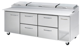 A large stainless steel Pizza Prep Table with four drawers, two compartment doors, and three-section covered top refrigerated storage. The unit is on wheels for mobility, featuring the True brand name on the right side.