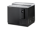 A commercial bottle cooler with a stainless steel top, side-mounted refrigeration, a sliding glass lid, built-in bottle opener, and vented section at the bottom right. The unit sits on a solid base for efficient beverage storage and chilling.