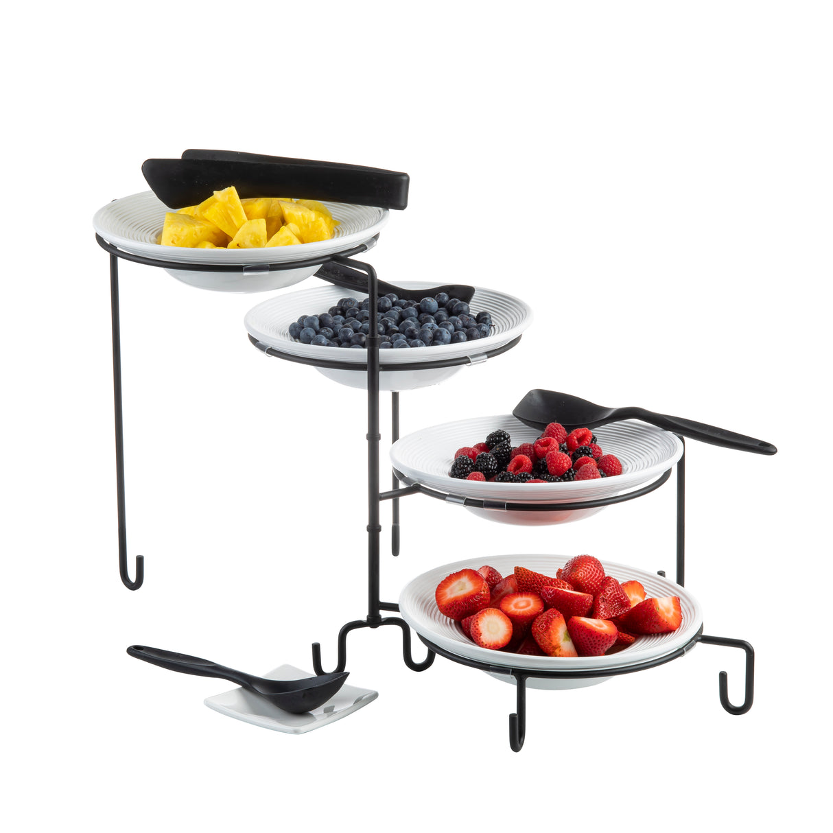 Four white bowls with pineapple, blueberries, mixed berries, and halved strawberries are displayed on a four-tiered black powder coated metal stand. Each bowl has a serving spoon, and slip resistant sleeves ensure stability at the base.