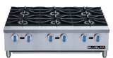 A commercial stainless steel gas range with six large black burners, blue and silver control knobs, and BLUELA branding on the lower right front panel. The countertop surface is clean, featuring a modern and industrial design.