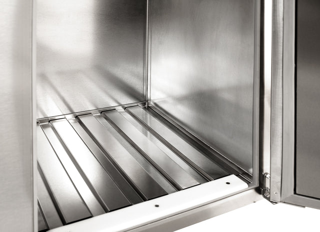 A close-up view of the inside of a stainless steel appliance, possibly featuring a keg floor rack, shows clean, shiny metal surfaces, a grooved bottom panel, and an open door on the right side. The interior appears empty and well-maintained.