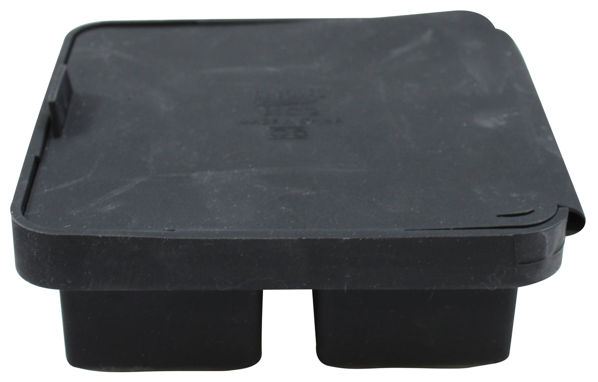 A black, rectangular plastic cover—possibly from an ice cube tray—with two protruding sections underneath. The lid appears slightly warped at one corner, and there is some embossed text on top, though it is not fully legible.