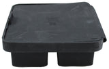 A black, rectangular plastic cover—possibly from an ice cube tray—with two protruding sections underneath. The lid appears slightly warped at one corner, and there is some embossed text on top, though it is not fully legible.